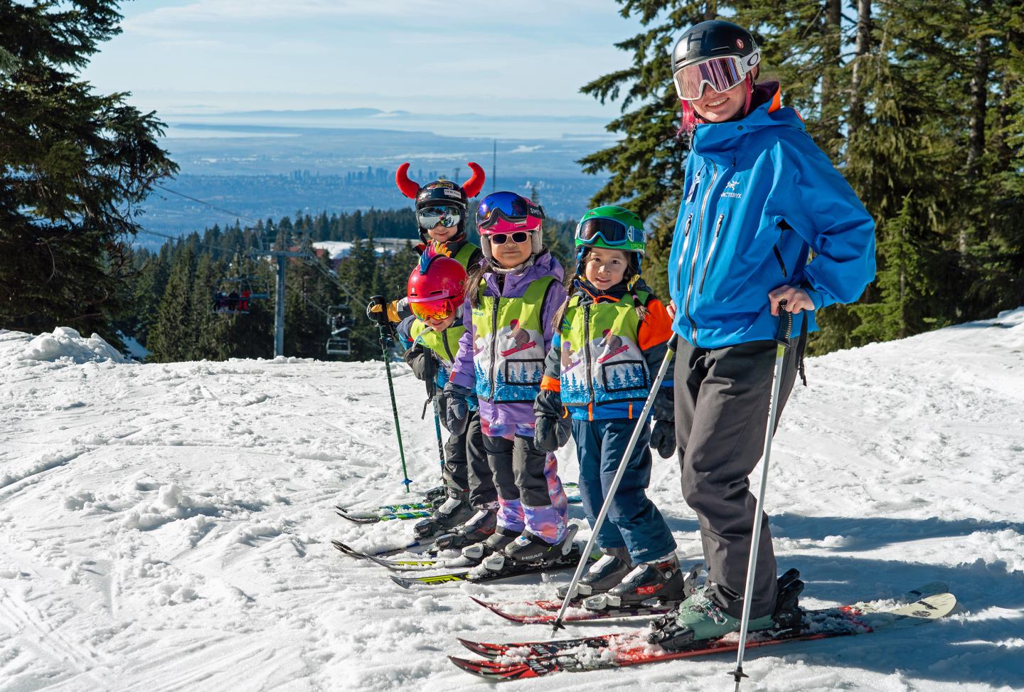 Ski instructor with four children on a snowy slope, wearing colorful ski gear.